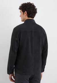 Schwarze Wildlederjacke mit Kragen, langen Ärmeln und Knopfmanschetten. Verfügt über eine glatte Textur und minimale Details auf der Rückseite.