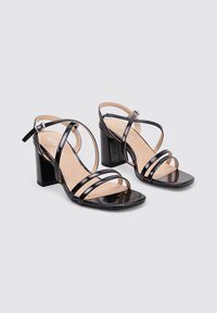 Sandalias de tacón cuadrado de charol negro con múltiples correas finas, punta cuadrada y una correa en el tobillo ajustable con hebilla plateada.