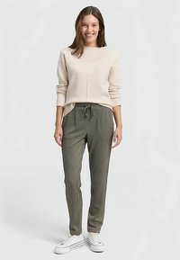 Pulover bej cu decolteu rotund și mâneci lungi, asortat cu pantaloni jogger verzi cu model și adidași albi. Pantalonii jogger au talie elastică.