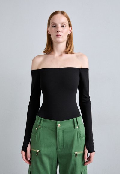 Bodysuit noir à épaules dénudées avec des manches longues, associé à un pantalon cargo vert présentant des détails zippés et une fermeture par bouton, mettant en valeur un design ajusté.