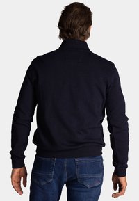 Marineblauwe trui met een hoge kraag, geribde manchetten en zoom, gemaakt van een zachte brei. Gedragen over blauwe denim jeans.
