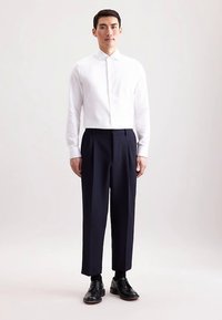 Wit shirt met lange mouwen en een hoge kraag, gecombineerd met donkerblauwe geplooide broek en zwarte veterlaarzen. Eenvoudig, klassiek ontwerp.