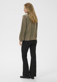 Lange mouwen, olijfgroene blouse met een gladde textuur en pofmouwen, gecombineerd met zwarte flared broek en zwarte schoenen.