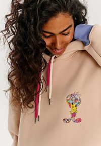 Beige mikina s ružovými a bielymi šnúrkami, na hrudi s farebnou karikatúrou. Mäkká tkanina a voľný strih.
