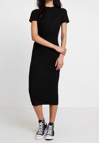 Robe midi noire à côtes, à manches courtes, avec une silhouette ajustée. Associée à des baskets montantes blanches pour créer un contraste.