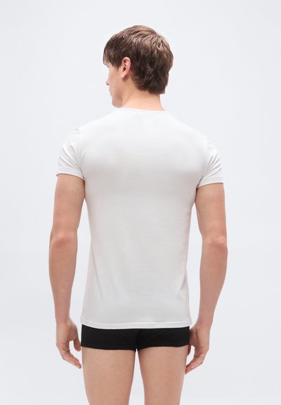 Λευκό κοντομάνικο μπλουζάκι από μαλακό ύφασμα, με στρογγυλή λαιμόκοψη και εφαρμοστή σχεδίαση, φορεμένο με μαύρο σορτς.