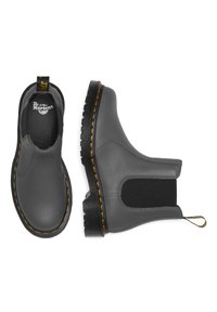 Botas chelsea de cuero gris con paneles laterales elásticos, costuras amarillas distintivas y una suela de goma negra texturizada.