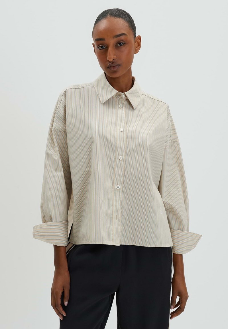 Beige button-up shirt with subtle vertical stripes, oversized fit, and cuffed sleeves. Made from smooth fabric with a classic collar design.