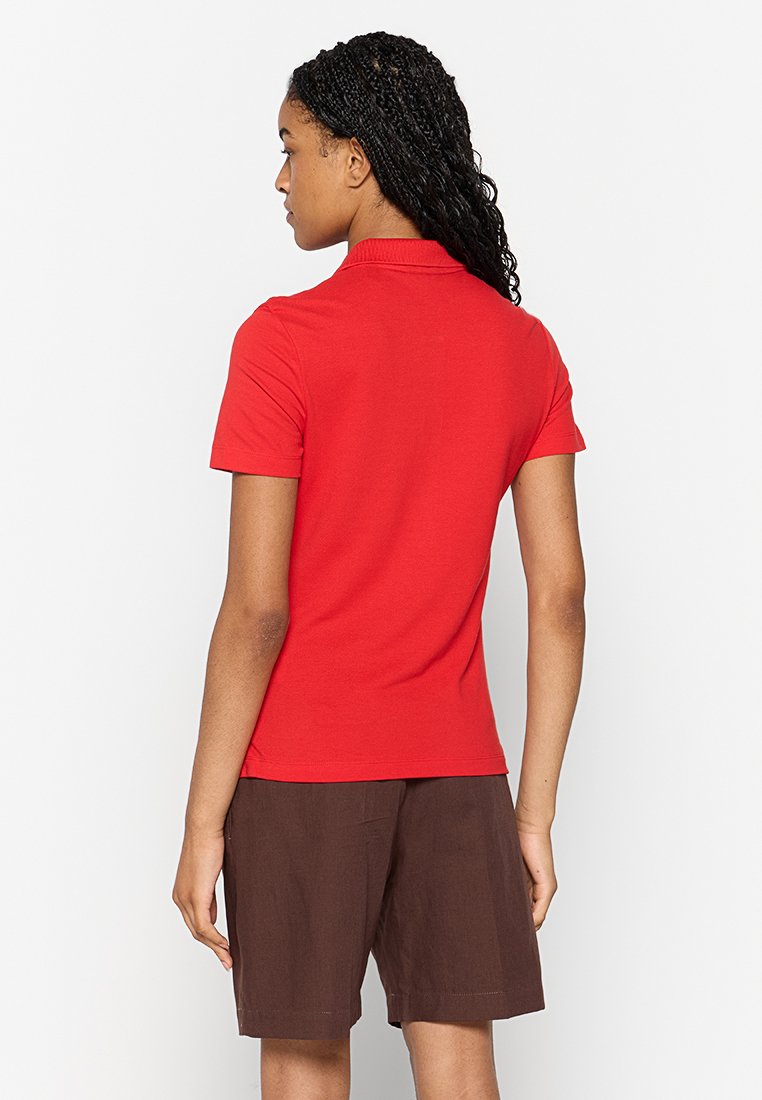 Camisa polo roja de manga corta con cuello, hecha de algodón. La vista posterior muestra un diseño ajustado. Combinada con pantalones cortos marrones para contraste.