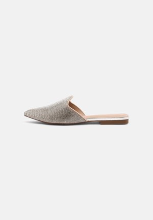 Slip-on flad sko med spids tå, pyntet med glitrende rhinsten og lille brun hæl på en lysegrå baggrund.