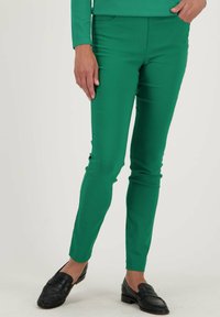 Groene, slim-fit broek met een gladde textuur en een elastische tailleband. Gecombineerd met zwarte instappers, die een op maat gemaakt ontwerp en strakke lijnen tonen.