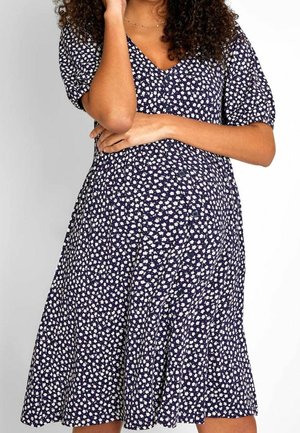 Laivastonsininen mekko, jossa valkoinen kukkakuvio, lyhyet pussihihat, V-aukko ja vyötärölle laskostettu kangas. Edessä nappikoristelu.