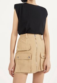 Svart kortärmad t-shirt i kombination med en beige cargoskirt som har två framfickor, silverdragkedja och ringdetalj vid midjan.