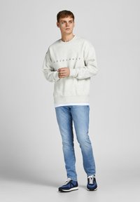 Light gray sweatshirt with "ORIGINALS" text, blue denim jeans, and navy blue sneakers with white accents. Casual outfit displayed on a model.