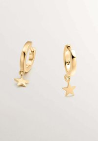 Pendientes de aro de oro con un acabado pulido y un pequeño charm de estrella colgando de cada pendiente. Diseño circular, textura suave.