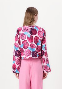 Cropped long-sleeve top with a vibrant floral pattern in pink and burgundy, featuring blue leaves on a light pink background.