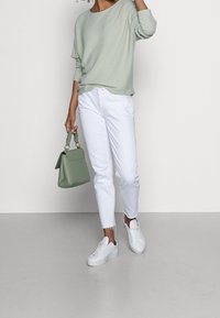 Ljusgrön ribbad tröja, vita avsmalnande jeans, vita sneakers och en grön handväska. Anmärkningsvärda detaljer: texturerat tyg, handväska med handtagsögla.