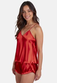 Rode satijnen pyjama-set met een v-hals cami-top met verstelbare bandjes en bijpassende shorts, gladde textuur en een gelaagd ontwerp.