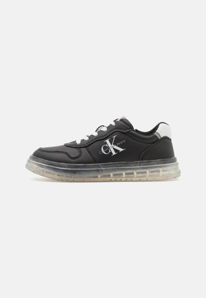 Czarny niskoprofilowy sneaker z białymi sznurowadłami, przezroczystą podeszwą oraz logo "Calvin Klein Jeans" z boku i białym akcentem przy pięcie.