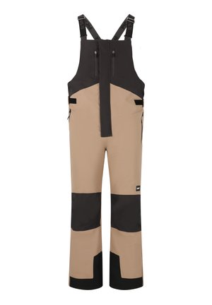Salopette impermeabile con un design beige e nero, realizzata in materiale resistente, dotata di spallacci regolabili e tasche con zip.