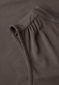 Detalle de una camisa de algodón gris que presenta una manga fruncida y una textura suave, con costuras limpias y un escote redondeado.