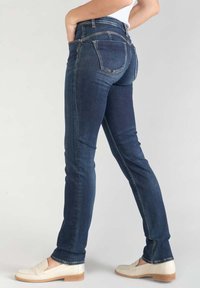 Vaqueros azul oscuro de corte slim, con cinco bolsillos y costuras sutiles. Combinados con mocasines blancos, que exhiben un diseño clásico.
