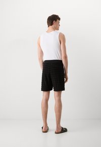 Zwarte textuurshorts met verticale strepen, gecombineerd met een witte tanktop. De outfit heeft een eenvoudig ontwerp en wordt aangevuld met zwarte sandalen.