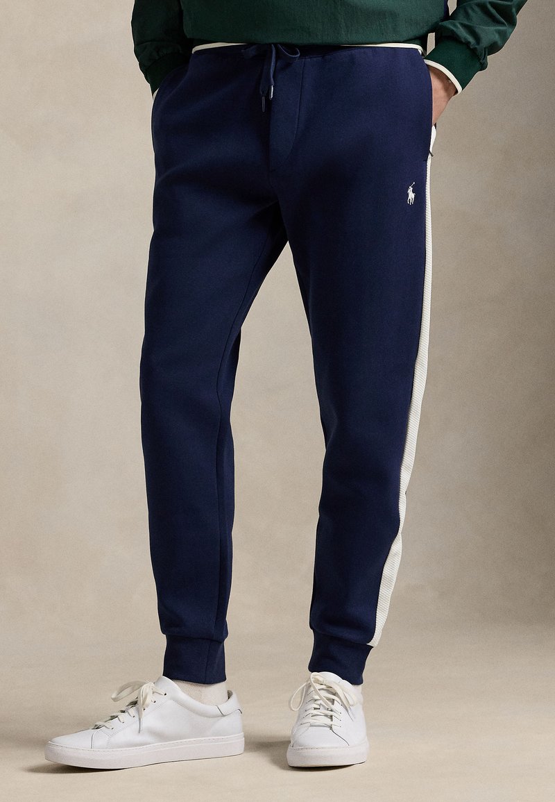 Mörkblå mjukisbyxor i bekvämt tyg med vita sidostripes, avsmalnande ben och resår i midjan med dragsko.