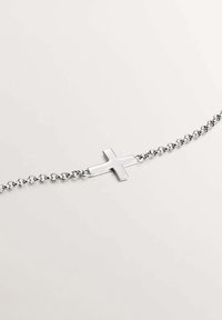Pulsera de cadena de plata con un colgante central de crucifijo metálico. Presenta una superficie lisa y un diseño de eslabones ovalados que refleja la luz.