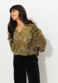 Blouse verte à motifs avec des manches à volants, dotée d'un décolleté en V. Assortie à un pantalon en velours côtelé noir. Texture lisse, détails d'impression complexes.