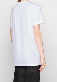 Bílý bavlněný tričko s krátkým rukávem, kulatým výstřihem a rovním lemem. Tkanina vypadá hladce a mírně se pružně. 