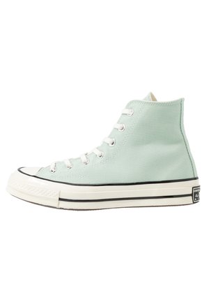 Vihreäsävyinen korkeavartinen kangaskenkä, jossa valkoinen kuminen kärkiosa, nauhat ja pohja, musta reunus ja Converse All Star -logo kantapäässä.