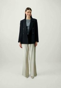Double-breasted black blazer over a gray top, paired with light beige wide-leg trousers. Simple design with minimal accents and classic lines.