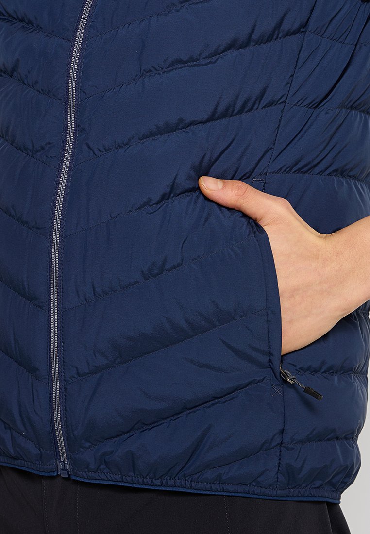 Marineblauer Steppweste mit diagonalen Quiltlinien, Frontreißverschluss und versteckten Seitentaschen. Glatte Textur mit elastischem Saum und minimalem Zubehör.