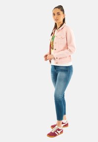 Chaqueta de mezclilla rosa claro, camiseta blanca con diseño de piña, jeans ajustados azules y zapatillas deportivas rojas y blancas con suelas de goma.