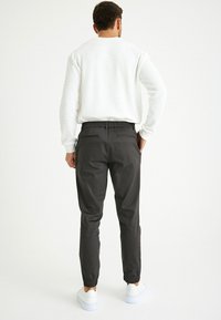 Graue elastische Hose mit umgeschlagenen Knöcheln, kombiniert mit einem weißen strukturierten Sweatshirt. Weiße Sneaker vervollständigen das Outfit.
