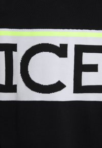 Tissu noir avec une bande horizontale blanche présentant de grandes lettres noires « ICE » et une fine bande jaune néon au-dessus de la bande.