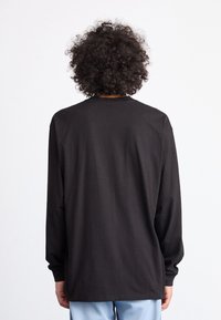Black long-sleeve shirt in a relaxed fit, made of smooth fabric. Features a crew neckline and straight hem. Back view shows simple design.