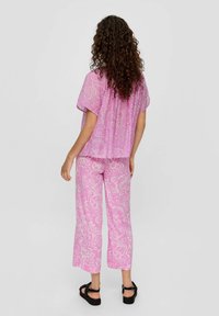 Blouse à motifs floraux roses à manches courtes et pantalon large assorti. Tissu doux avec une texture légère. Sandales noires complètent la tenue.