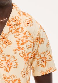 Korte mouwen overhemd van lichtgele stof, met grote oranje bloemenpatronen, een spitse kraag en een relaxte pasvorm.