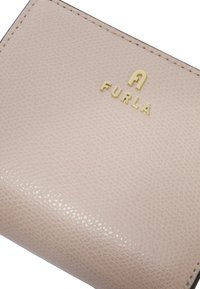 Portefeuille en cuir rose clair avec une finition texturée. Logo doré en relief "FURLA" sur le devant. Design épuré et minimaliste.