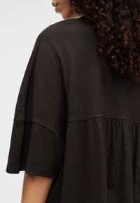 Dark brown, loose-fit top with short sleeves, featuring a rounded neckline and a flared, gathered lower section. Soft, textured fabric.