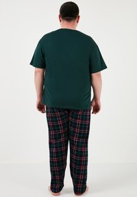 Miesten pyjama-setti, joka sisältää tummanvihreän puuvillapaidan ja ruudulliset flanellihousut vihreänä, punaisena ja mustana, jossa on joustava vyötärö.