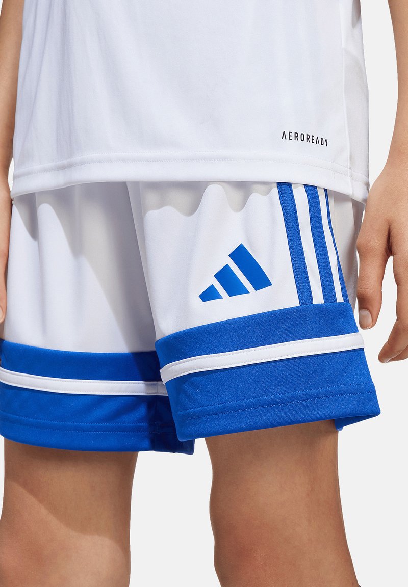 Shorts de sport blancs et bleus avec logo Adidas bleu et trois bandes, portés avec un haut blanc AEROREADY sur la partie inférieure du torse et les jambes d’une personne.