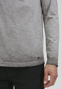 Langærmet grå skjorte med en gradient effekt, struktureret stof og et lille logopatch ved den nederste kant. Enkel, tætsiddende design.