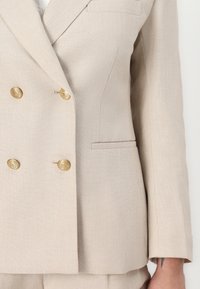 Beige dobbeltradet blazer laget av teksturert stoff, med detaljer i gulltone, en brystlomme og skreddersydde slag.