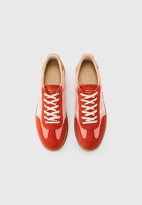 Red and pink suede sneakers with white accents, round toes, striped design, and beige inner lining. Features cream laces and rubber soles.