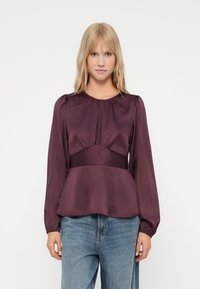 Burgundy satin blouse with long puff sleeves, gathered neckline, and a peplum hem; paired with light blue denim jeans.