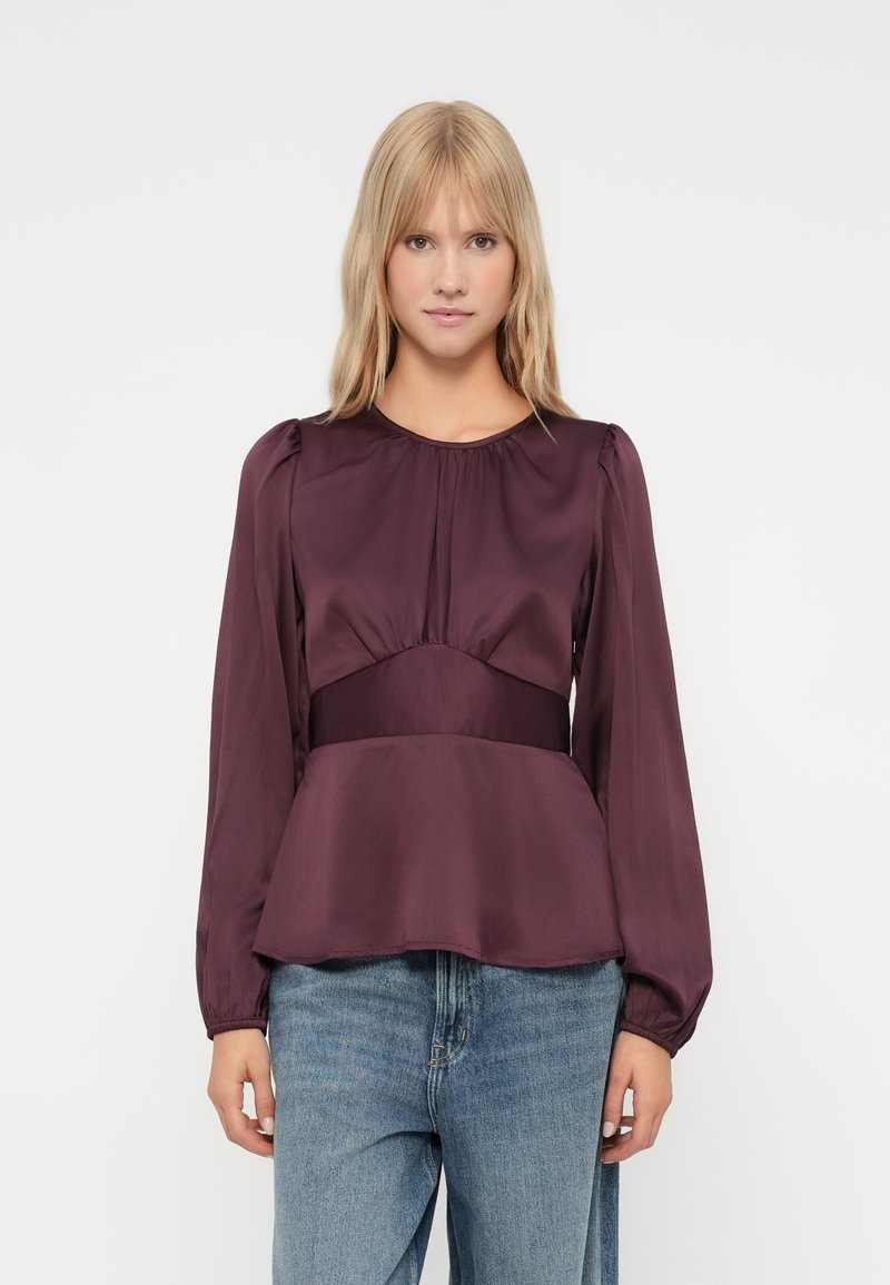 Burgundy satin blouse with long puff sleeves, gathered neckline, and a peplum hem; paired with light blue denim jeans.