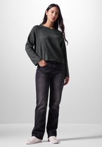 Dunkelgrauer, kürzer geschnittener Pullover mit langen Ärmeln, kombiniert mit schwarzen geraden Jeans und hellen Sneakers. Einfaches und lässiges Outfit.